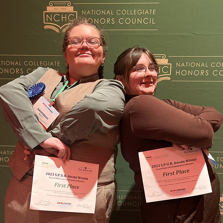 Two students posing for the camera, holding their conference award certificates.